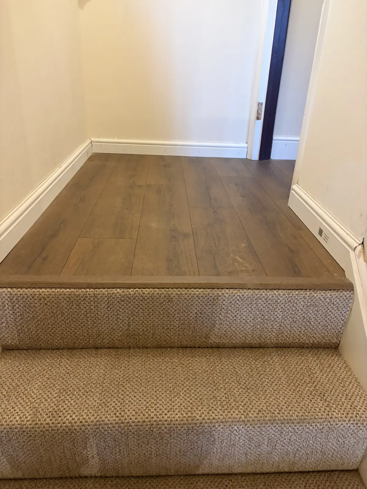 Carpeted stairs meeting an oak-effect laminate landing