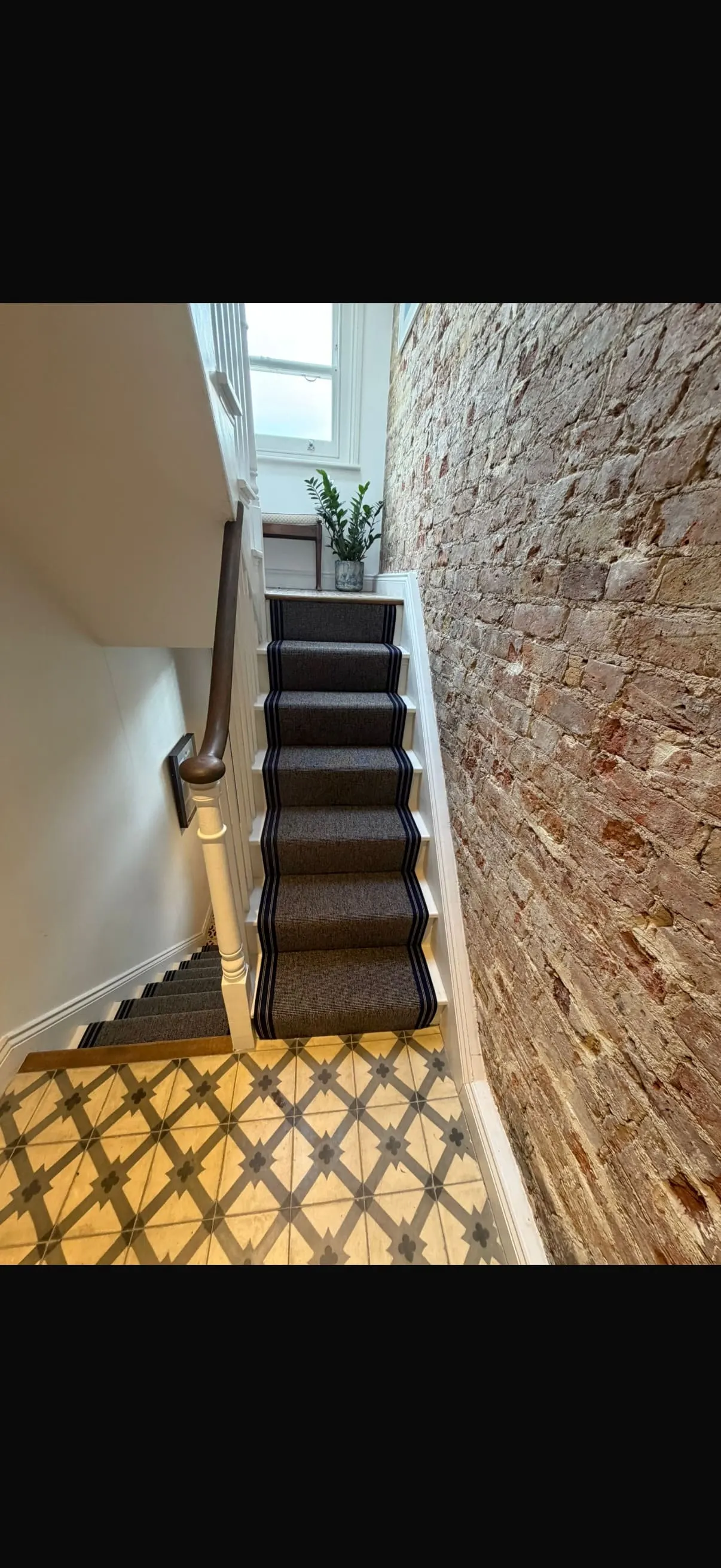 Dark stair runner with striped border on a staircase beside an exposed brick wall
