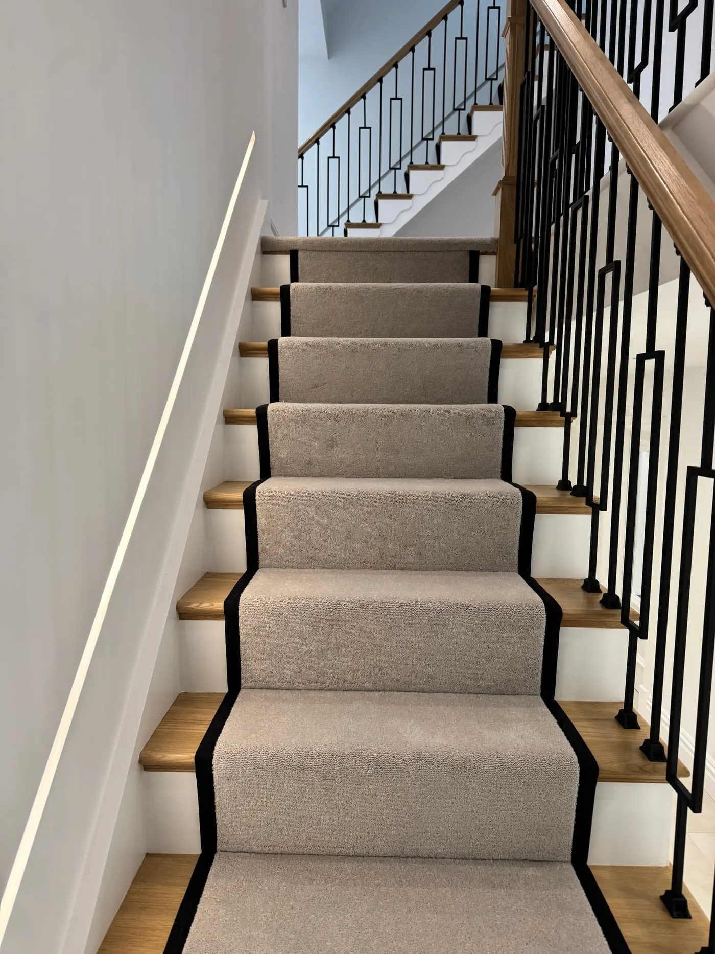 Pale grey stair runner with black border on an oak staircase with black metal spindles