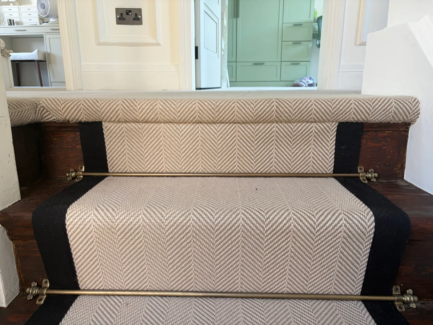 Close detail of herringbone stair runner with black border and brass stair rods