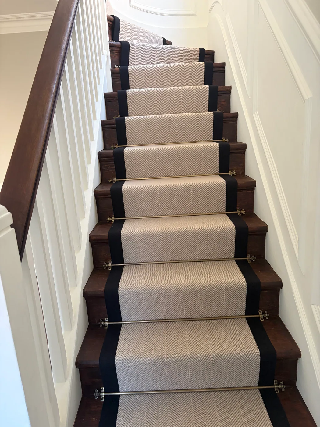 Herringbone stair runner with black border and brass stair rods fitted on dark timber stairs