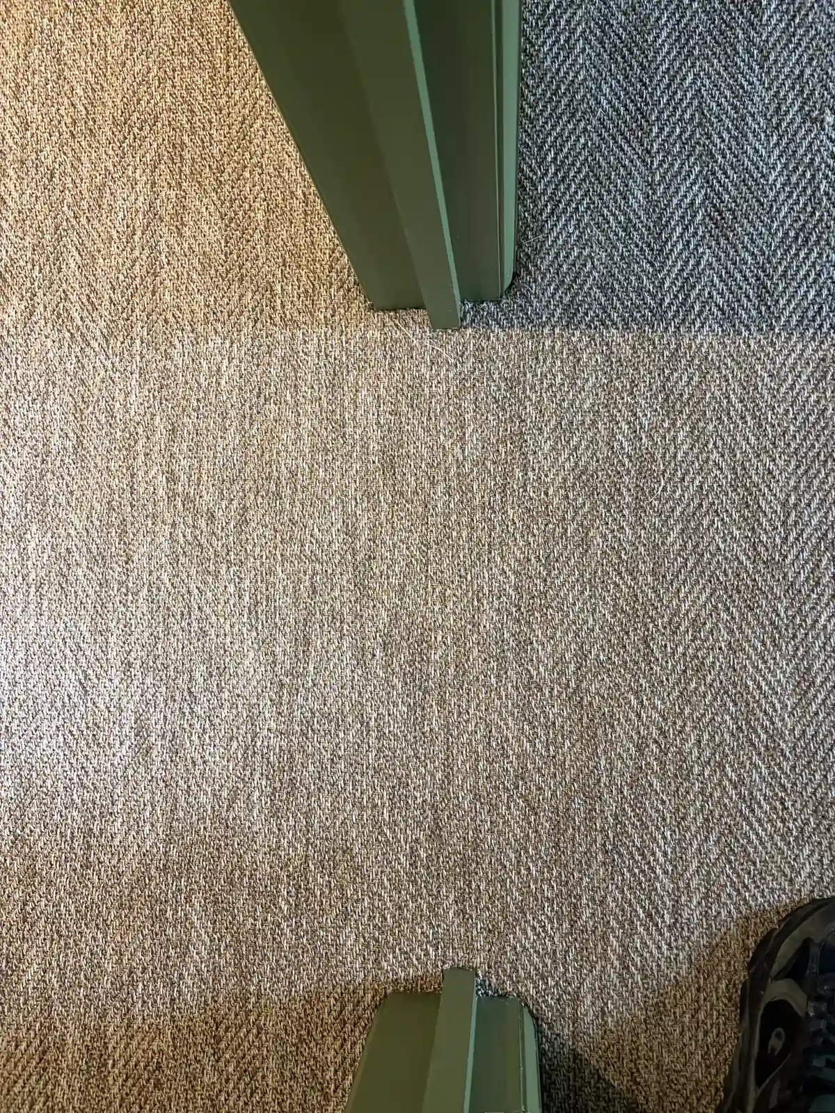 Close-up of natural loop carpet meeting grey herringbone flooring at a doorway