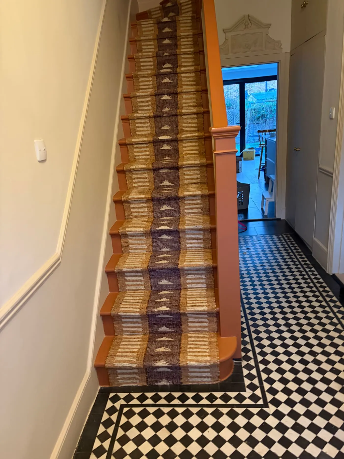Patterned stair runner leading down to a black-and-white tiled hallway