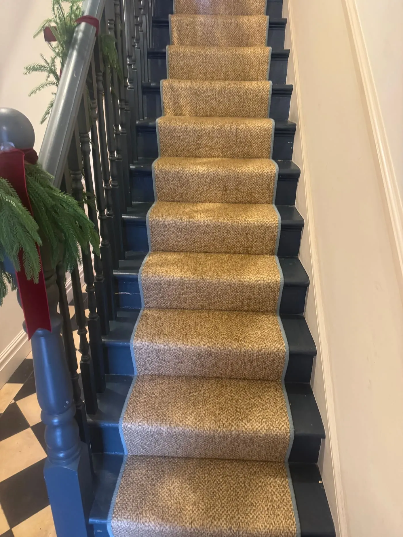 Natural sisal-style stair runner with dark border above a black-and-white tiled hallway
